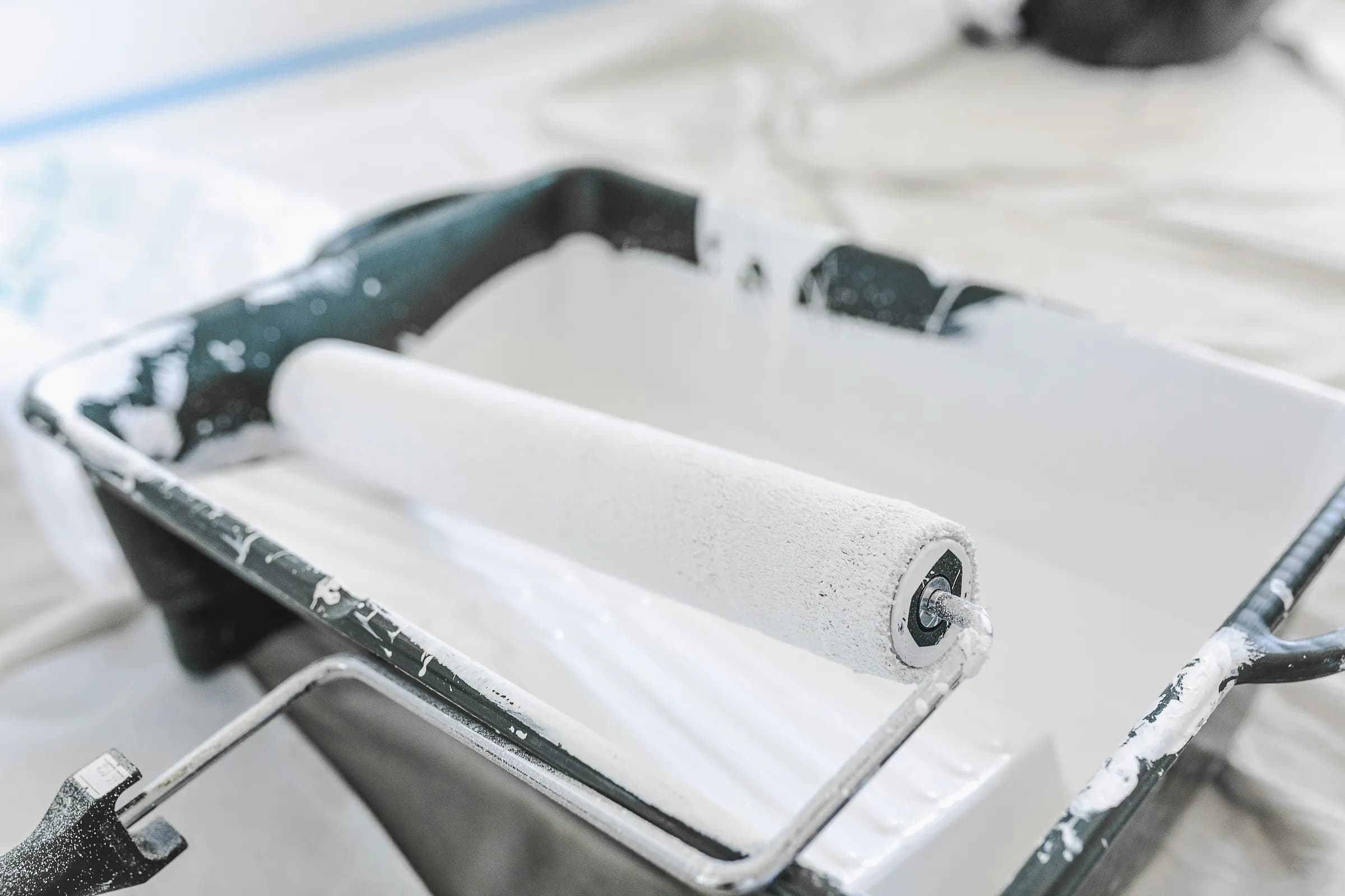 Paint roller resting in a tray of white paint on a drop cloth
