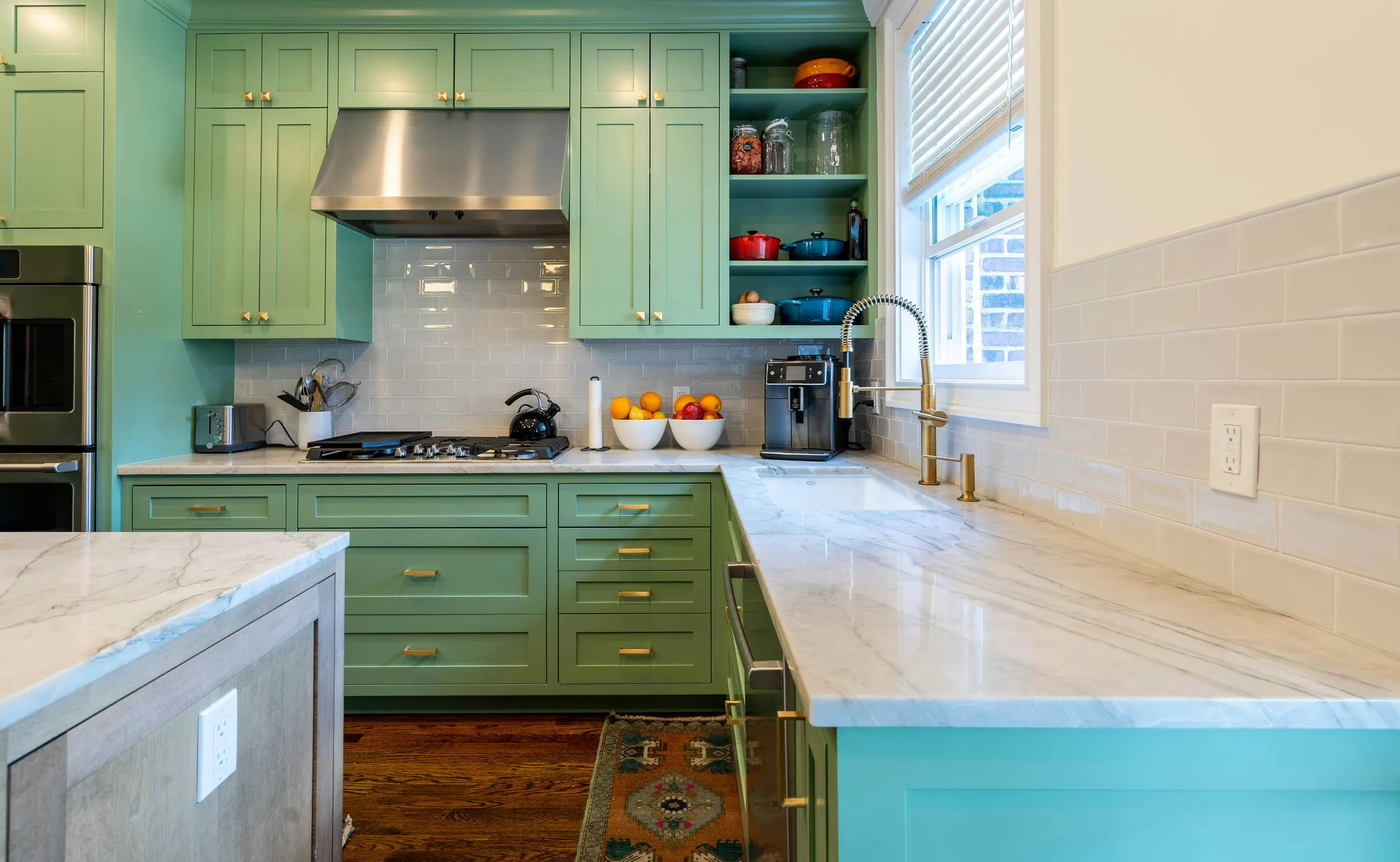 Kitchen with sage-green painted shaker cabinets, brass hardware and marble countertops