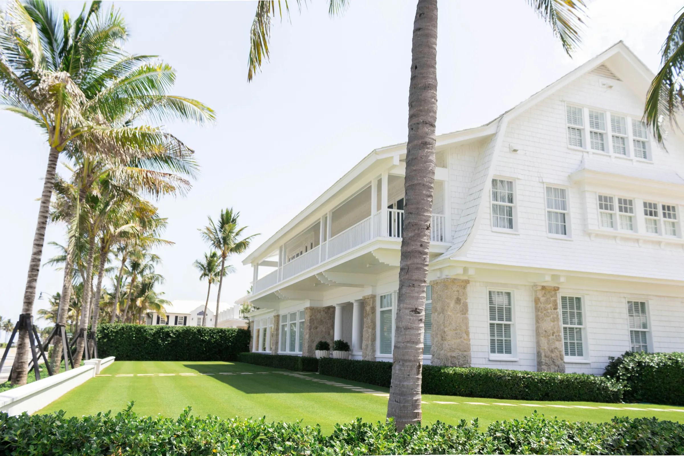 White two-story coastal home framed by tall palm trees and a striped green lawn