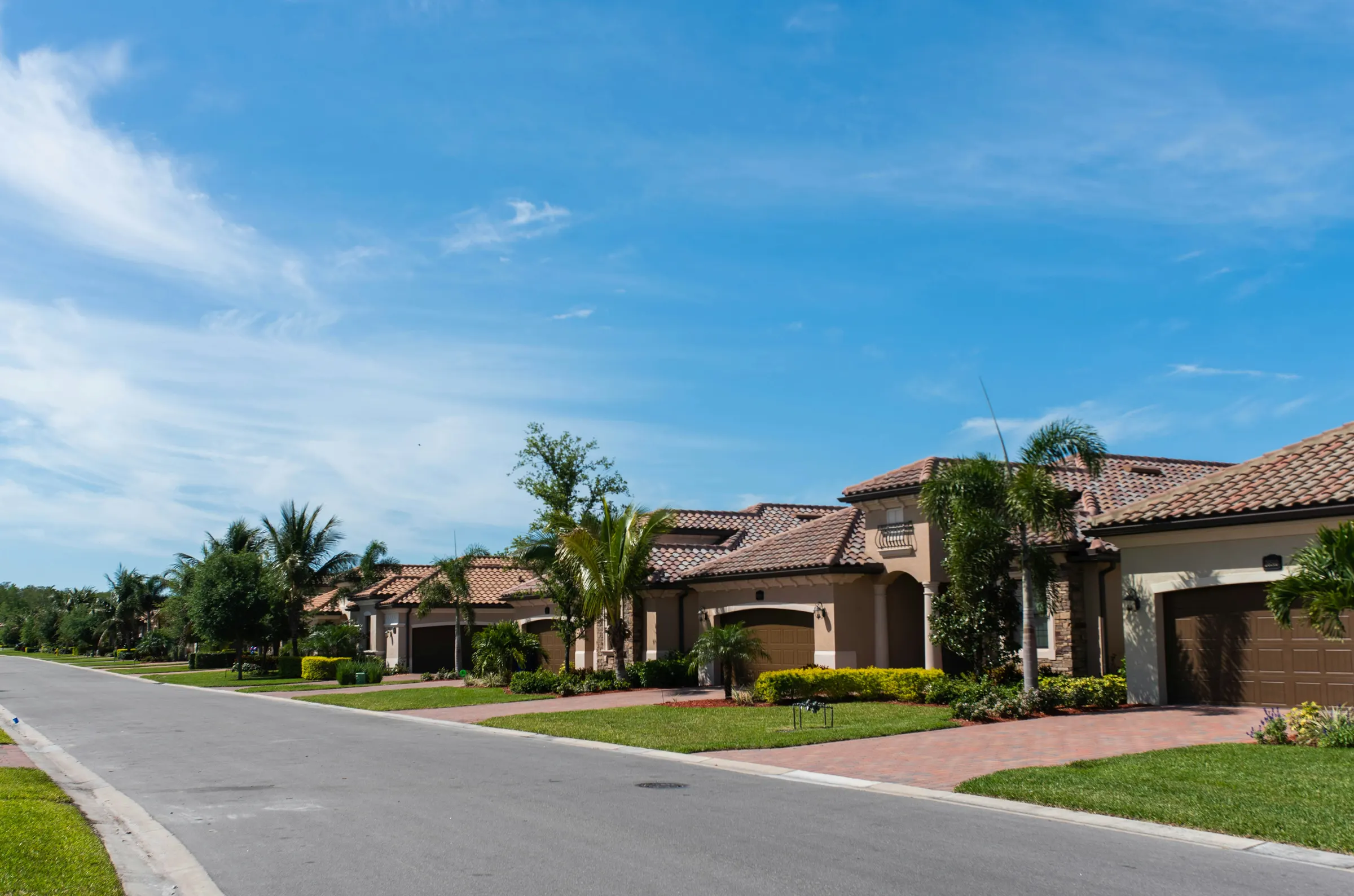 Row of Florida stucco homes with tile roofs, palm trees and manicured lawns under a blue sky