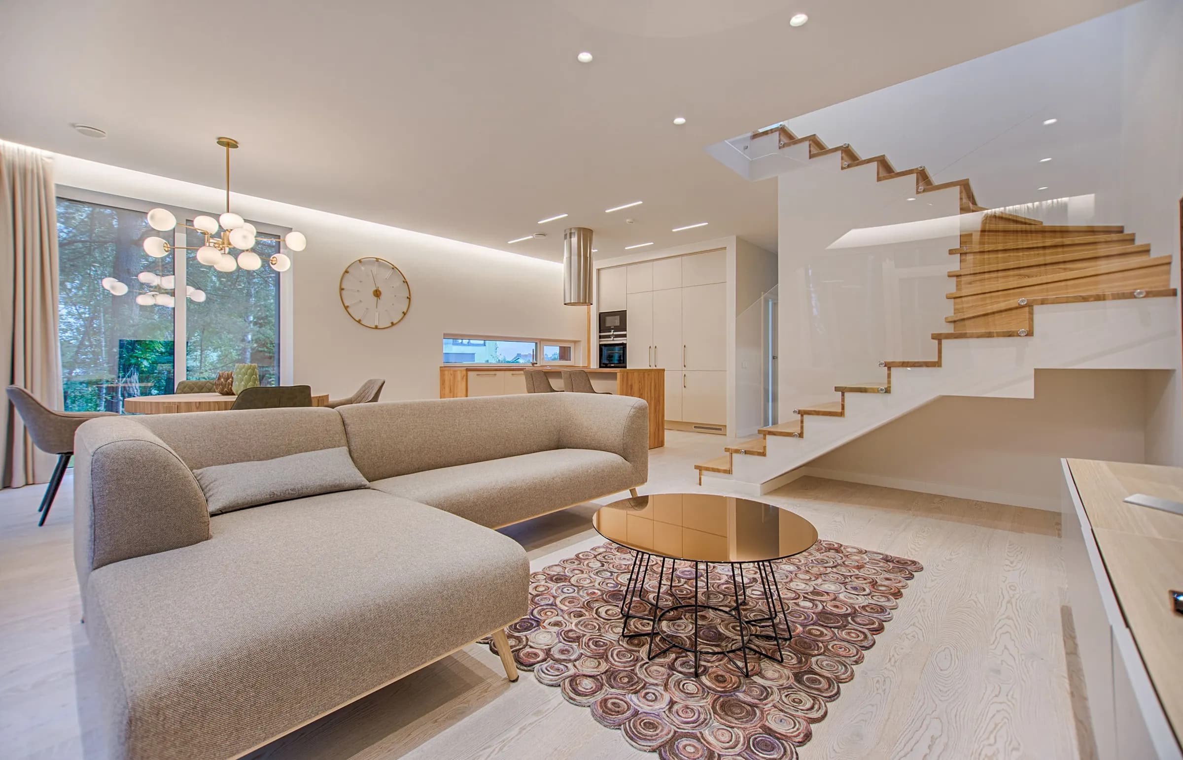 Bright open living room with warm white walls, a neutral sectional and a floating wood staircase